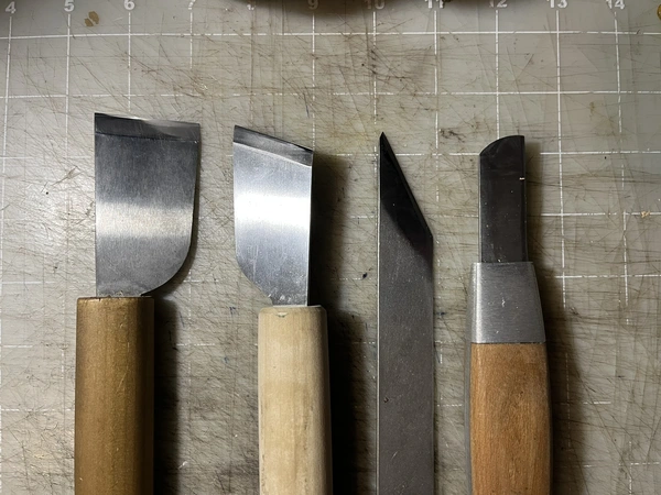 photo of a lineup of knives showing progressively more parallel angles of edges to handle axes